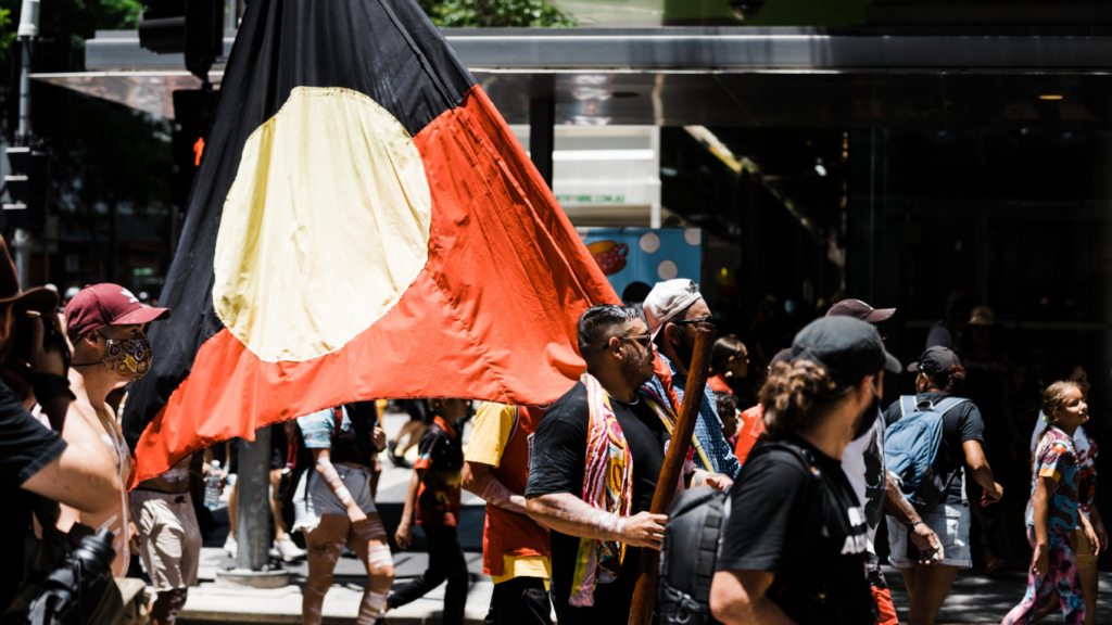 A wide shot of people marching down a city street carrying a flag.