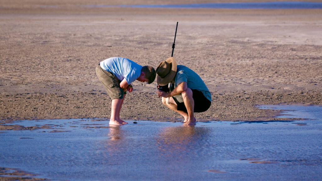 Photo of father and son on fishing trip looking into a rockpool or shallow part of ocean.