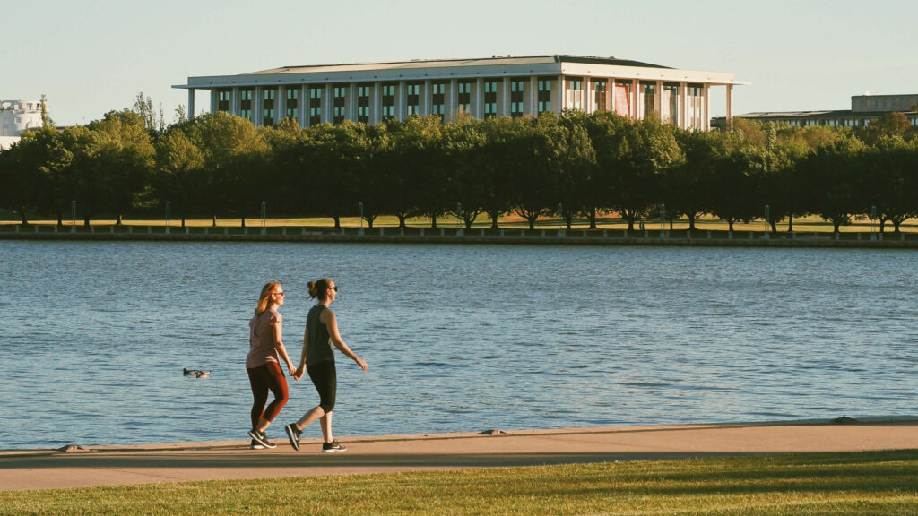 Two women walking in fit gear beside water.