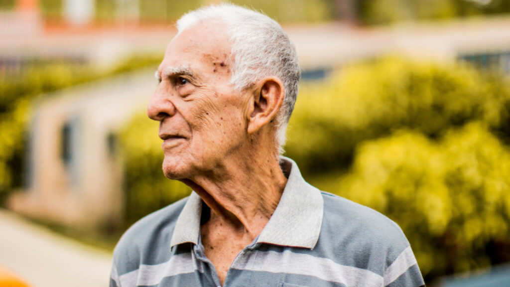 Portrait of man looking serious into the distance with a green bush behind him.