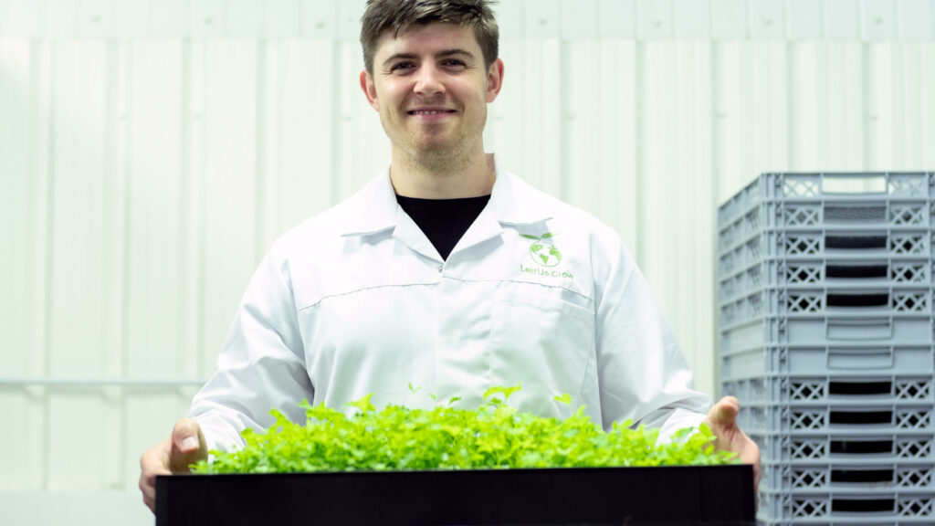 Photograph of man looking to camera and holding a tray of plants.