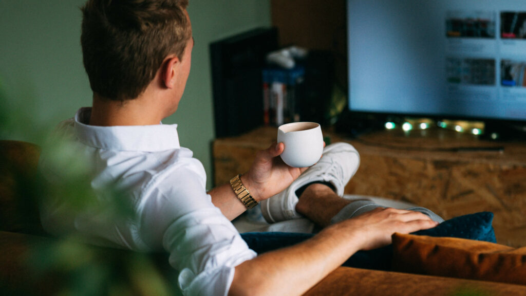 Photograph of man watching television with coffee mug in hand.