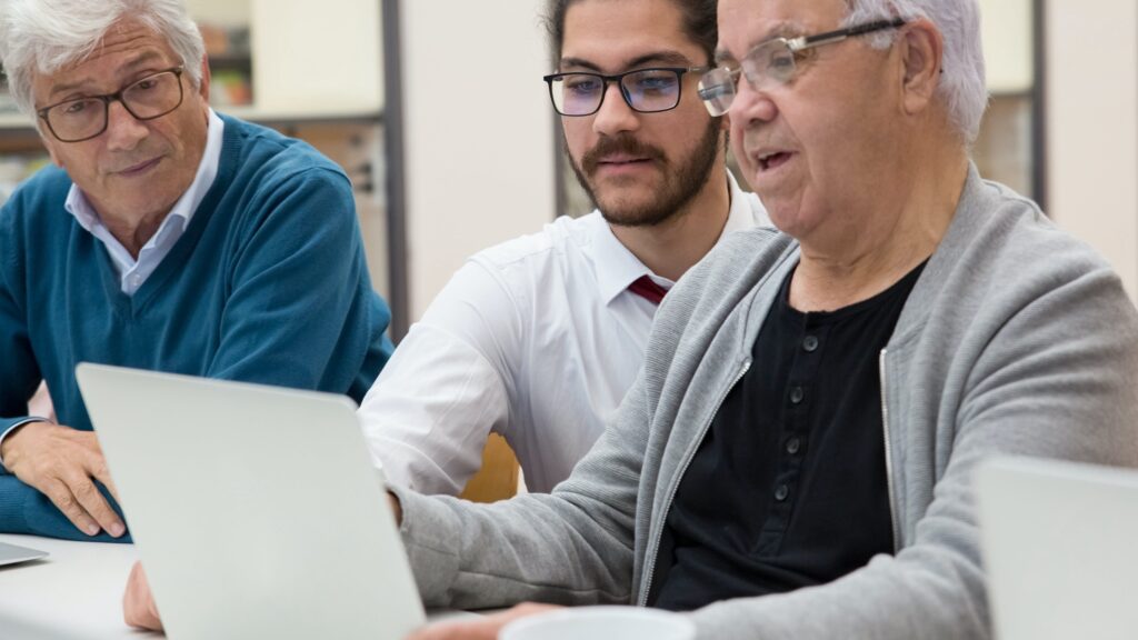 Photo of three men in glasses sitting at a desk looking at a laptop computer.