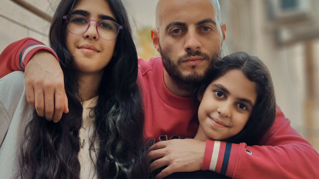 A father and two daughters looking to camera in embrace.