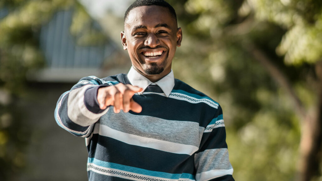 Photograph of a man point towards camera and smiling.