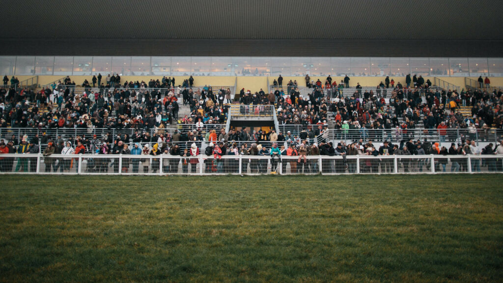 Wide photograph of a large crowd watching a horse race.