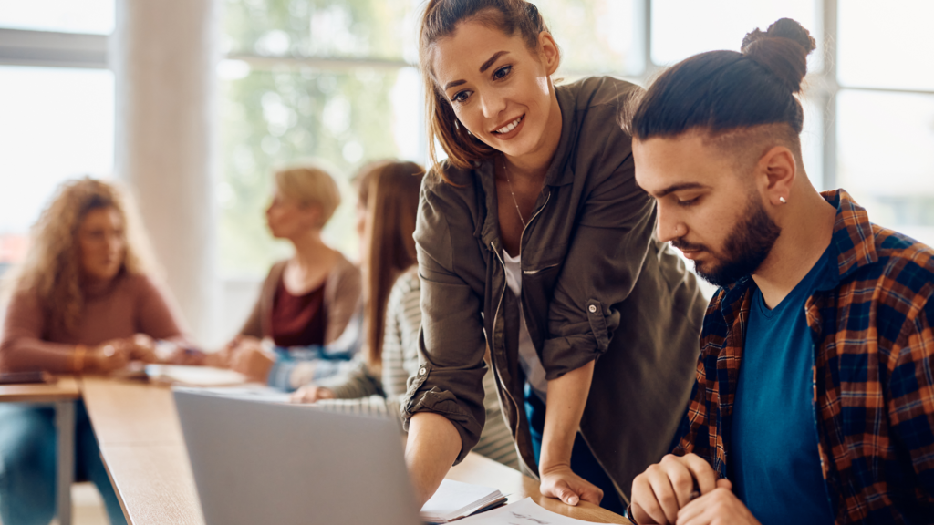 Image of young-adult learners in classroom setting focus on two people looking at a laptop