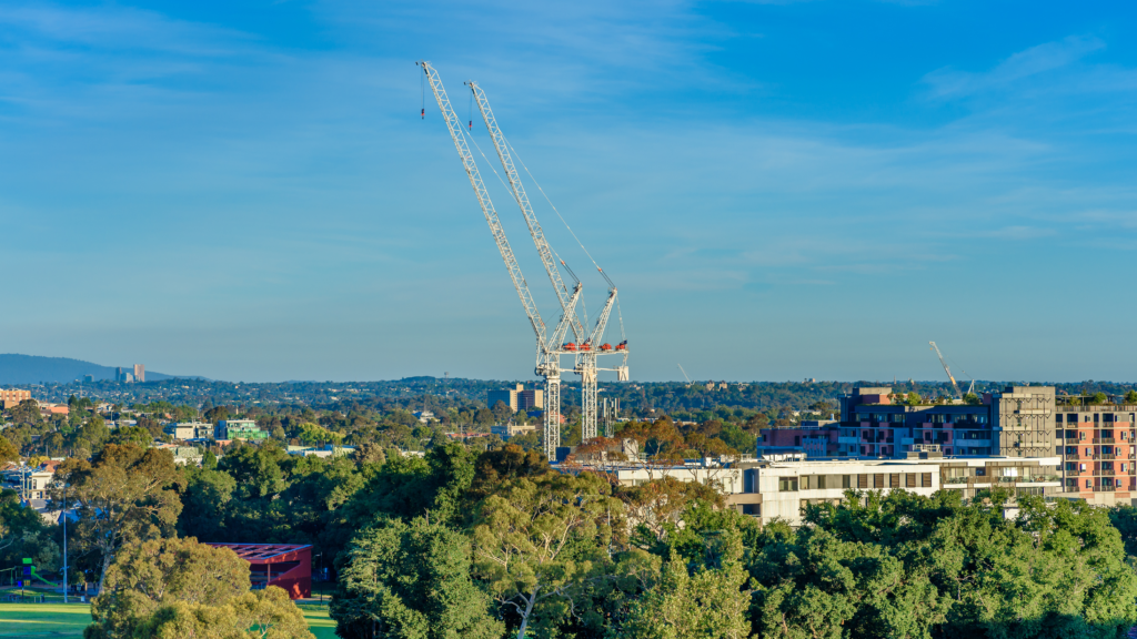 Melbourne, Australia, A suburban apartment development under construction with two large cranes against a blue sky with white clouds.