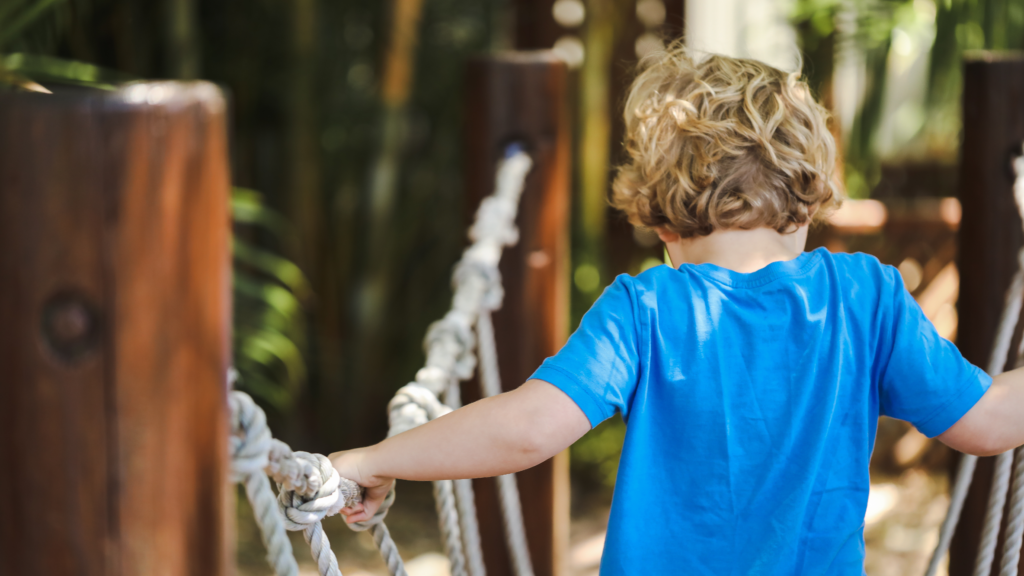 Preschool child playing on rope swing in beautiful tropical kindergarten yard.